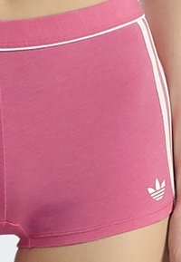 Gros plan sur des shorts de sport roses avec des rayures blanches sur les côtés et un petit logo Adidas blanc près de l'ourlet.