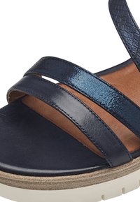Sandalo in pelle blu navy con tre cinturini, caratterizzato da una finitura lucida e una fascia testurizzata. Piattaforma in sughero e plantare liscio in colore a contrasto.