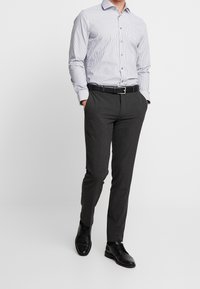 Herroutfit med en ljusblå och vitrandig skjorta med knappar, mörkgrå byxor samt ett svart läderskärp och skor.