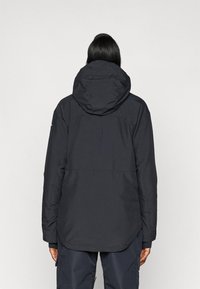 Chaqueta con capucha de color gris oscuro, hecha de material resistente al agua, con un corte holgado, tejido texturizado y capucha ajustable para mayor protección.