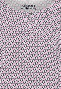 Short-sleeve blouse in white fabric featuring a repeating pink and navy geometric pattern, with a small placket and a rounded neckline.