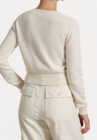 Světlý béžový pletený svetr s žebrovaným límcem a manžetami, s přiléhavým lemem. Zadní část zdobí texturovaný vzor a volný střih.