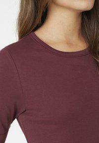 Burgundivörös, puha, rugalmasságot biztosító pamutból készült, testhez simuló felső, kerek nyakkivágással és rövid ujjakkal, sima textúrával és megerősített varrásokkal.
