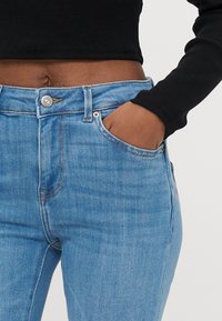 Ανοιχτό μπλε τζιν με ψηλή μέση, διαθέτει κλείσιμο με ασημένιο κουμπί, μπροστινές τσέπες και ελαφριά ελαστικότητα στο ύφασμα.