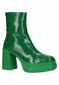 Botín de tobillo brillante en verde oscuro con suela de plataforma y tacón cuadrado, textura suave, vista lateral sobre fondo blanco.