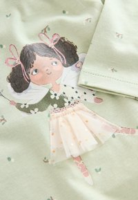 Svetlo zelená látka s potlačenou postavičkou s kučeravými vlasmi a ružovými mašľami, ozdobenou tylovou sukňou a kvetinovými doplnkami.