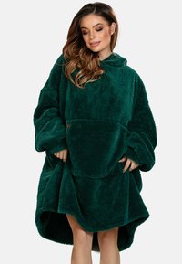 Hoodie oversize verde bosco realizzato in materiale morbido e peluche. Presenta una grande tasca frontale e un cappuccio ampio.