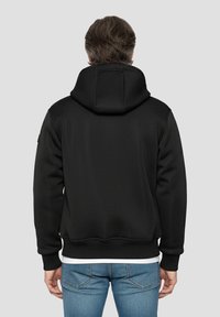 Zwarte sweater met capuchon van een gestructureerde stof, met geribbelde manchetten en zoom. Heeft een relaxte pasvorm, gezien vanaf de achterkant, gecombineerd met een blauwe spijkerbroek.