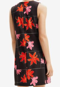 Černé šaty bez rukávů s živými červenými a růžovými květinovými vzory, které mají jemný čtvercový design a zadní zip.