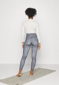 Legginsy o wysokim stanie, dopasowane, w czarno-biały kratkę, zestawione z długim białym topem, na macie do jogi.