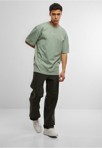 Green cotton oversized t-shirt with a white line graphic, paired with loose black jeans and white sneakers. Simple design and relaxed fit.