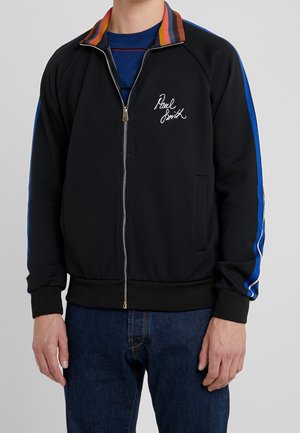 Veste noire zippée avec col rayé multicolore et détails latéraux bleus. Comprend une poche avant et un logo signature sur la poitrine.