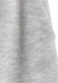 Tissu gris clair en gros plan avec un logo brodé "4F" subtil en fil ton sur ton en bas à droite.