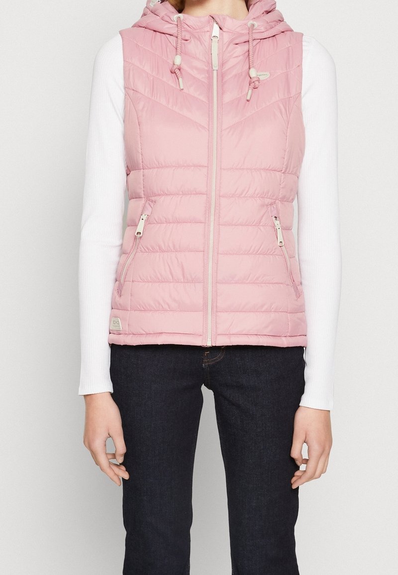 Rosa pufferväst med huva, med en kviltad design, framzipper och två sidofickor. Bärs över en långärmad vit skjorta.