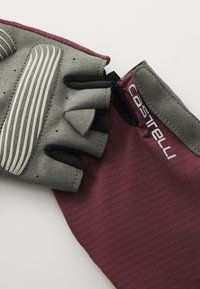 Guantes de ciclismo sin dedos con un cuerpo elástico color marrón burdeos, palma acolchada gris con rayas verticales blancas y tiradores negros para facilitar su puesta.