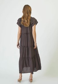 Rochie maxi maro închis cu mâneci fluture, cu pliuri și o siluetă fluidă. Fabricată dintr-un material ușor, cu o textură moale.