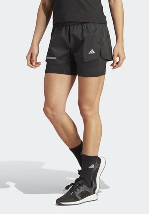 Pantalones cortos deportivos negros con tela ligera, cintura elástica y diseño en capas. Combinados con zapatillas negras y calcetas.