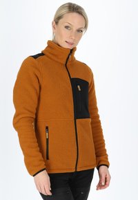 Giacca in pile arancione bruciato con accenti neri. Presenta un colletto alto, zip anteriore e tasca sul petto con materiale a contrasto.