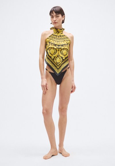 Črno kopalke z živopisno rumeno zgornjo obleko z vzorcem, ki ima visoko ovratnik in pentljo. Dizajn vključuje okrasne okrogle motive in zlato kovinsko opremo.