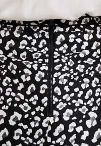 Tissu noir avec un motif léopard blanc, doté d'une fermeture éclair centrale et d'une texture lisse.