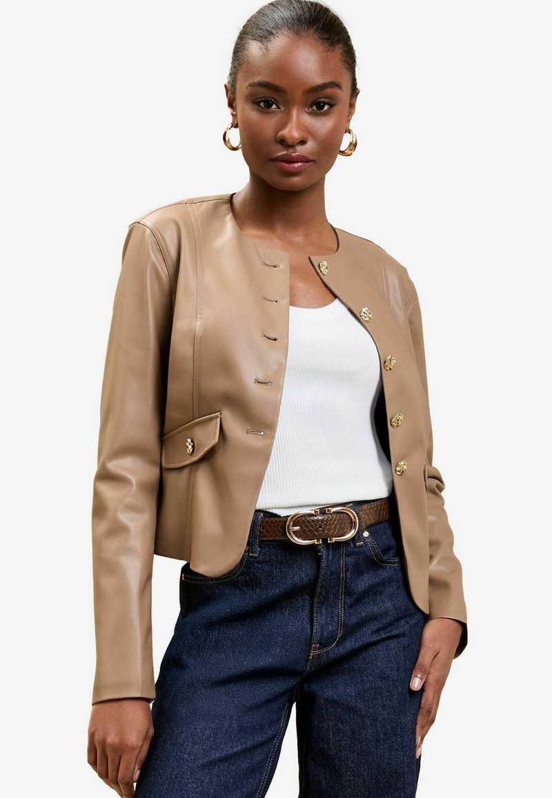 Giacca cropped in pelle color cuoio con hardware dorato, tasca singola e chiusura con bottone. Abbinata a un top bianco e jeans in denim scuri.