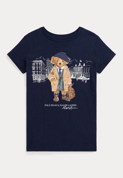 Camiseta de algodón color marino con un gráfico de un oso vestido con abrigo, sombrero y un bolso, con un fondo de paisaje urbano.