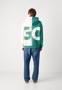 Mikina s kapucí v kombinaci smetanové a tyrkysové barvy s velkým nápisem „GO“; design s kapucí, texturovaná bavlněná tkanina, ve spojení s světle modrými džínami.