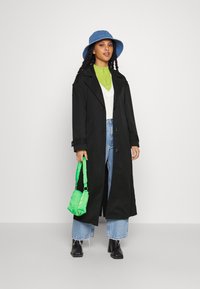 Svart lang frakk, grønn zip-up genser, hvit vest, blå denimjeans, svarte ankelstøvletter, og en grønn veske. Blå bøttehatt fullfører looken.