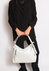 Grote witte handtas van textuurleer, voorzien van gouden hardware, een ritssluiting en een decoratieve hanger.