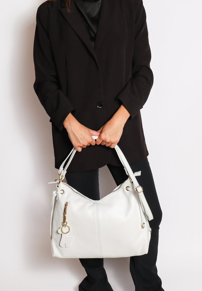 Grote witte handtas van textuurleer, voorzien van gouden hardware, een ritssluiting en een decoratieve hanger.