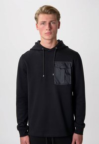 Felpa nera con cappuccio e maniche lunghe, dotata di una tasca in nylon sul petto con patta, cappuccio regolabile e una texture liscia.