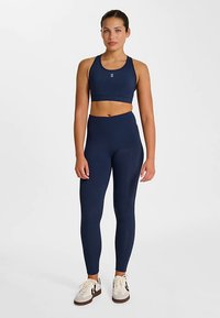 Marinblå sport-bh och högmidjade leggings i mjukt, stretchigt tyg, kombinerade med ljusa träningsskor. Enkla logodetaljer.