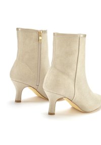 Botines beige de ante texturizado con cierre de cremallera en la parte posterior, que presentan un tacón de altura media y un ribete suave en contraste.