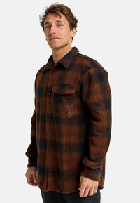 Flanellhemd in braun, grün und blau kariert. Mit Knöpfen, einer Brusttasche und einem strukturierten Stoff. Lange Ärmel mit geknöpften Enden.