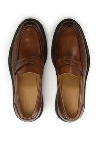 Mocasines de cuero marrón con un acabado suave, que presentan un diseño cosido en la parte superior y una suela de goma negra. Forro interior texturizado.