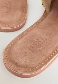 Kohvisuheline sandaal, millel on lame tald ja nähtav õmblus. Siseosa sisaldab reljeefset brändingut ja sileda tekstuuri.