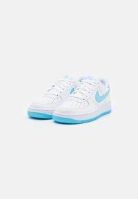 Fehér sportcipők világoskék kiegészítőkkel, perforált orrésszel, textúrált gumitalppal és kiemelkedő Nike logóval az oldalon.