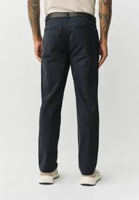 Dark navy chinos with a straight fit, featuring back pockets with button closures and a smooth texture, complemented by a black belt and light footwear.