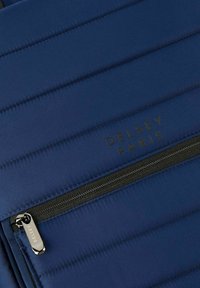 Zaino in tessuto blu navy con texture trapuntata verticale, dotato di una cerniera nera e dettagli in metallo con il logo "DELESEY PARIS" in oro.