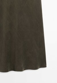 Mörk olivgrön flytande tyg med en slät textur och en lätt vågig fåll mot en enfärgad ljus bakgrund.