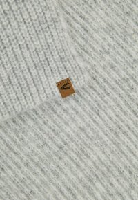 Gray knitted fabric with a textured pattern. Small brown leather tag with a logo is visible. The overall appearance is soft and cozy.