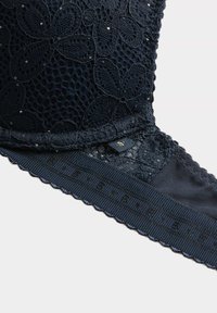 Navy blauw kant beha met bloemenpatroon, versierd met kleine kralen; heeft een textuurband en gegolfde randen voor extra detail.