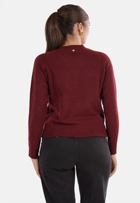 Maglione bordeaux con scollo rotondo, maniche lunghe, polsini e orlo a costine, con un piccolo dettaglio a forma di cuore al centro della schiena.