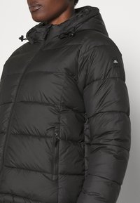 Chaqueta de plumas negra con capucha, que cuenta con cierre de cremallera, puños elásticos y un patrón texturizado y acolchado. Pequeño logo en la manga.