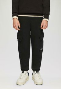 Schwarze Cargo-Hosen mit zwei seitlichen Taschen, elastischen Bündchen und einem kleinen Logo am Bein. Weiße Sneaker mit marineblauen Akzenten. Lässiges, bequemes Design.