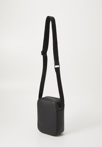 Black faux leather crossbody bag with a rectangular shape, zip closure, and adjustable strap, featuring a smooth texture and minimal design.