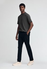 Graues T-Shirt mit kurzen Ärmeln, schwarze Hose und hellbeige Sneakers. Das lässig geschnittene T-Shirt hat eine dezente Grafik. Glatte Stoffqualität.