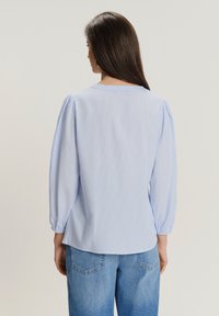 Blusa a righe blu chiaro con maniche a sbuffo, scollo rotondo e polsini elasticizzati. Indossata con jeans in denim chiaro a vita alta.