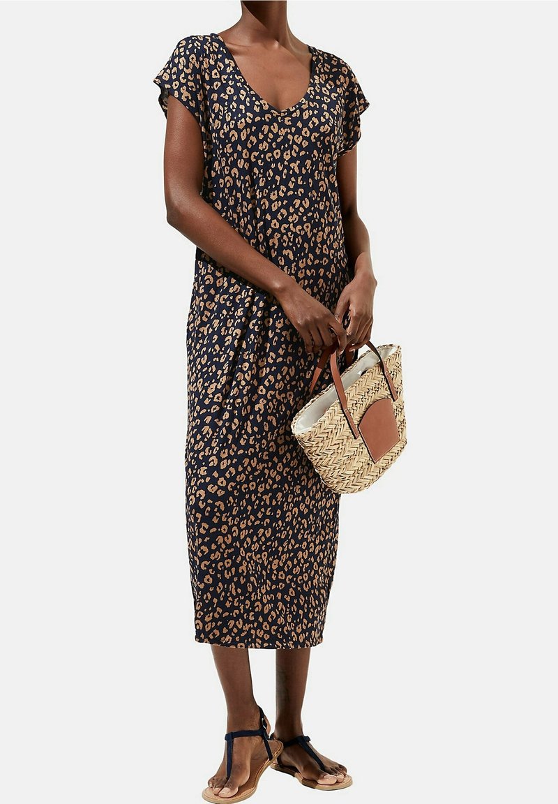 Femme portant une robe midi bleu marine avec un imprimé léopard beige, tenant un sac à main en paille tressée avec des détails en cuir marron et portant des sandales noires.