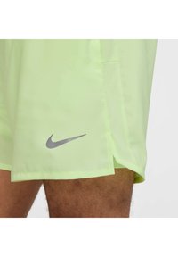 Vaaleanvihreät Nike-shortsit, joissa on hopeinen logo helmassa ja verkkopaneeli sivussa ilmanvaihtoa varten. Sujuva, kevyt kangas.